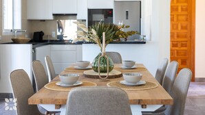 A modern kitchen with white cabinets, a wooden dining table with six grey chairs, and a vase with dried flowers. - Villa CELENZA by Abahana Villas (Benitachell)