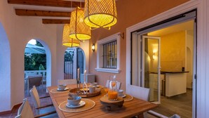 A dining area with a wooden table set for four, surrounded by wicker chairs. - Villa CELENZA by Abahana Villas (Benitachell)