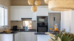 A modern kitchen with white cabinets, a black countertop, a stainless steel refrigerator, and a coffee maker. - Villa CELENZA by Abahana Villas (Benitachell)
