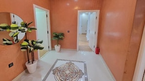 Un couloir avec un sol blanc, un tapis décoratif et des plantes en pot.