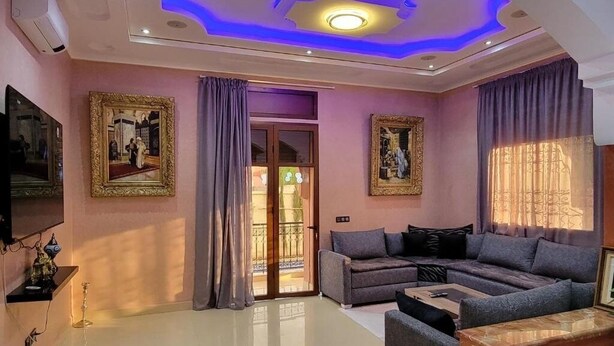 Un salon avec un canapé gris, une table basse et un téléviseur. Deux tableaux encadrés sont accrochés aux murs.