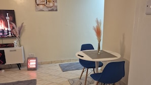 A dining area with a round table and blue chairs, a small heater, and a TV displaying a cityscape. - Double K Loft 1-bedroom apartment in Nairobi (Nairobi)