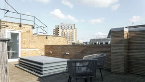 Eine Dachterrasse mit Holzdeck, zwei Korbstühlen und einem Glastisch.