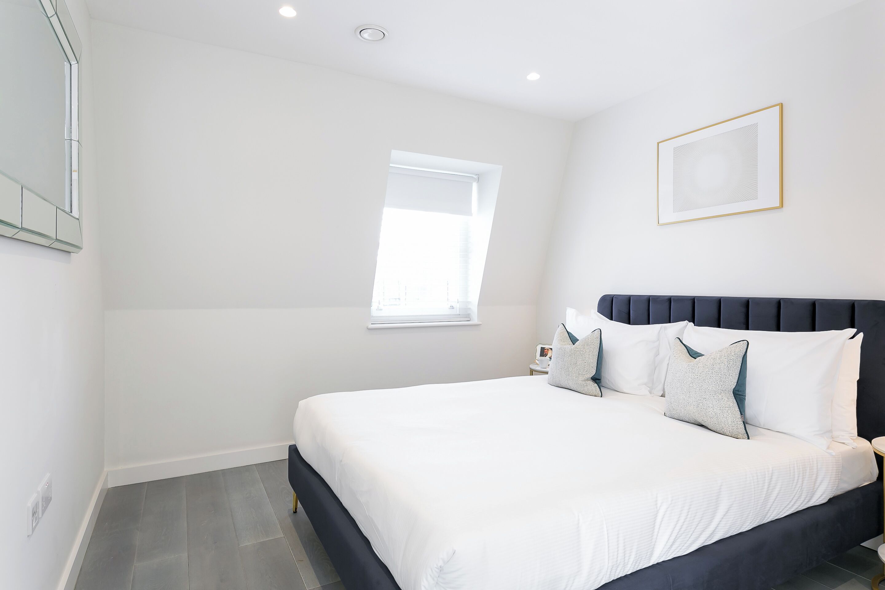 A modern bedroom with a large bed, a window, and a framed picture on the wall.