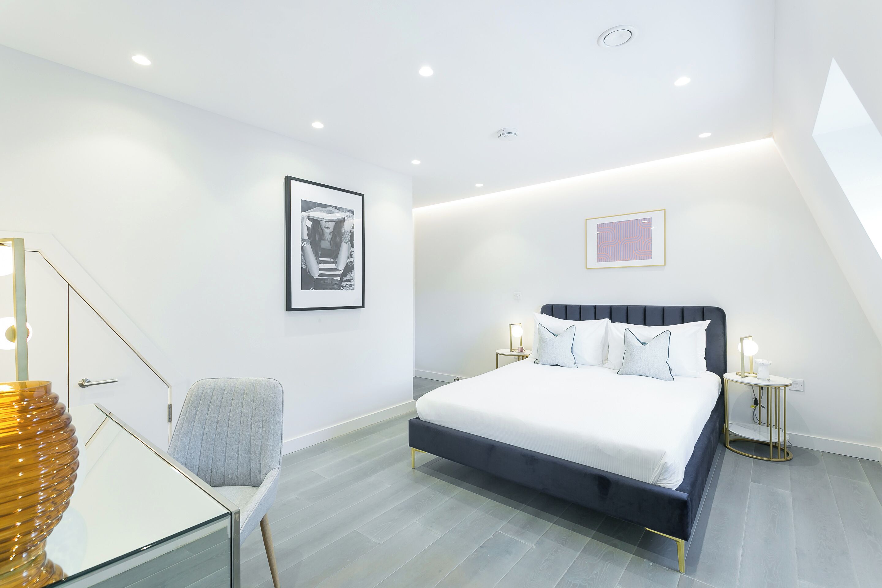 A modern bedroom with a bed, bedside tables, a chair, and artwork on the walls.