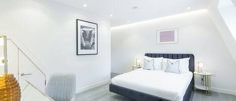 A modern bedroom with a bed, bedside tables, a chair, and artwork on the walls.