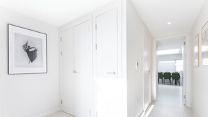 Ein Flur mit weißen Wänden, einem Schwarz-Weiß-Kunstwerk und Blick in einen Essbereich mit grünen Stühlen.
