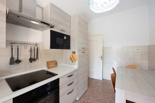 A modern kitchen with a microwave, stove, and utensils hanging on the wall.