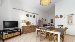 Un salon avec un téléviseur, une table à manger en bois, des chaises, une lampe et des éléments de décoration murale.