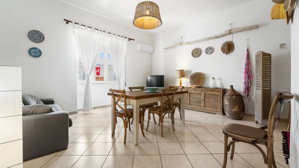 Un salon comprenant un canapé, une table à manger avec des chaises, un téléviseur et un luminaire suspendu.