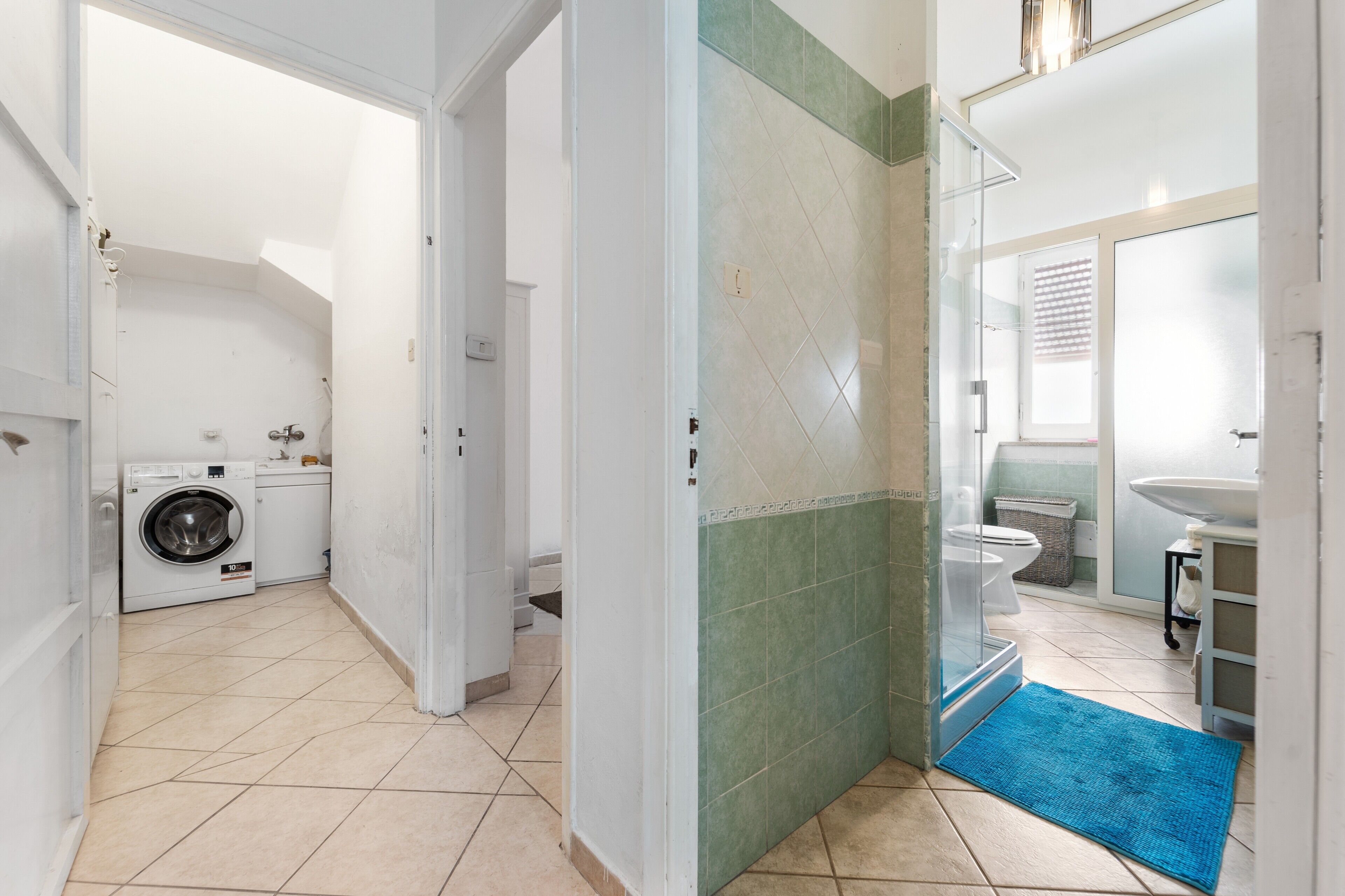 A laundry area with a washing machine, a bathroom with a toilet and sink, and a blue rug on the floor.