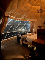 Habitación tipo tienda de campaña con una ventana grande, una cama, un escritorio y una lámpara colgante.