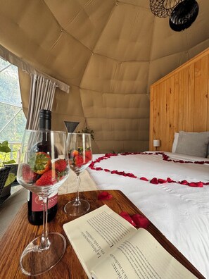 Ein Zeltraum mit Bett, einer Weinflasche, zwei Weingläsern mit Erdbeeren und einem offenen Buch.