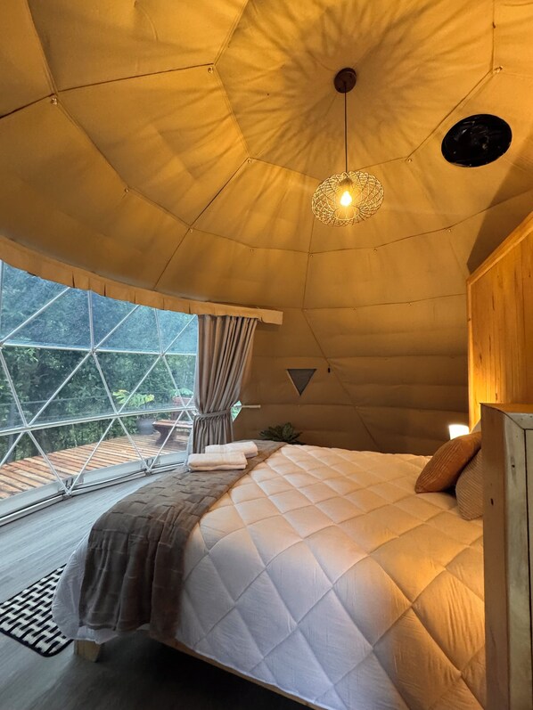 A tent-style room with a bed, a hanging light fixture, and a view through the window.