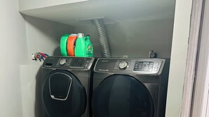 Une buanderie équipée de deux machines à laver à chargement frontal, d’un enrouleur de tuyau et d’un sèche-linge Samsung.