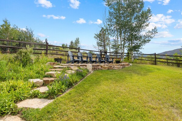 A fenced outdoor area with a stone pathway, a wooden fence, and a row of Adirondack chairs.