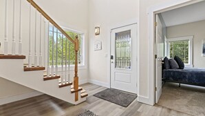 A spacious living area with a wooden staircase, a door with a window, and a bed with pillows.
