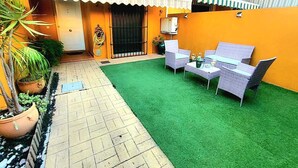 Eine Terrasse mit Kunstgrasanlage, Korbmöbeln und Topfpflanzen.