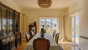 Une salle à manger avec une longue table, des chaises, un lustre et une vue dégagée sur l’extérieur grâce à de grandes fenêtres.
