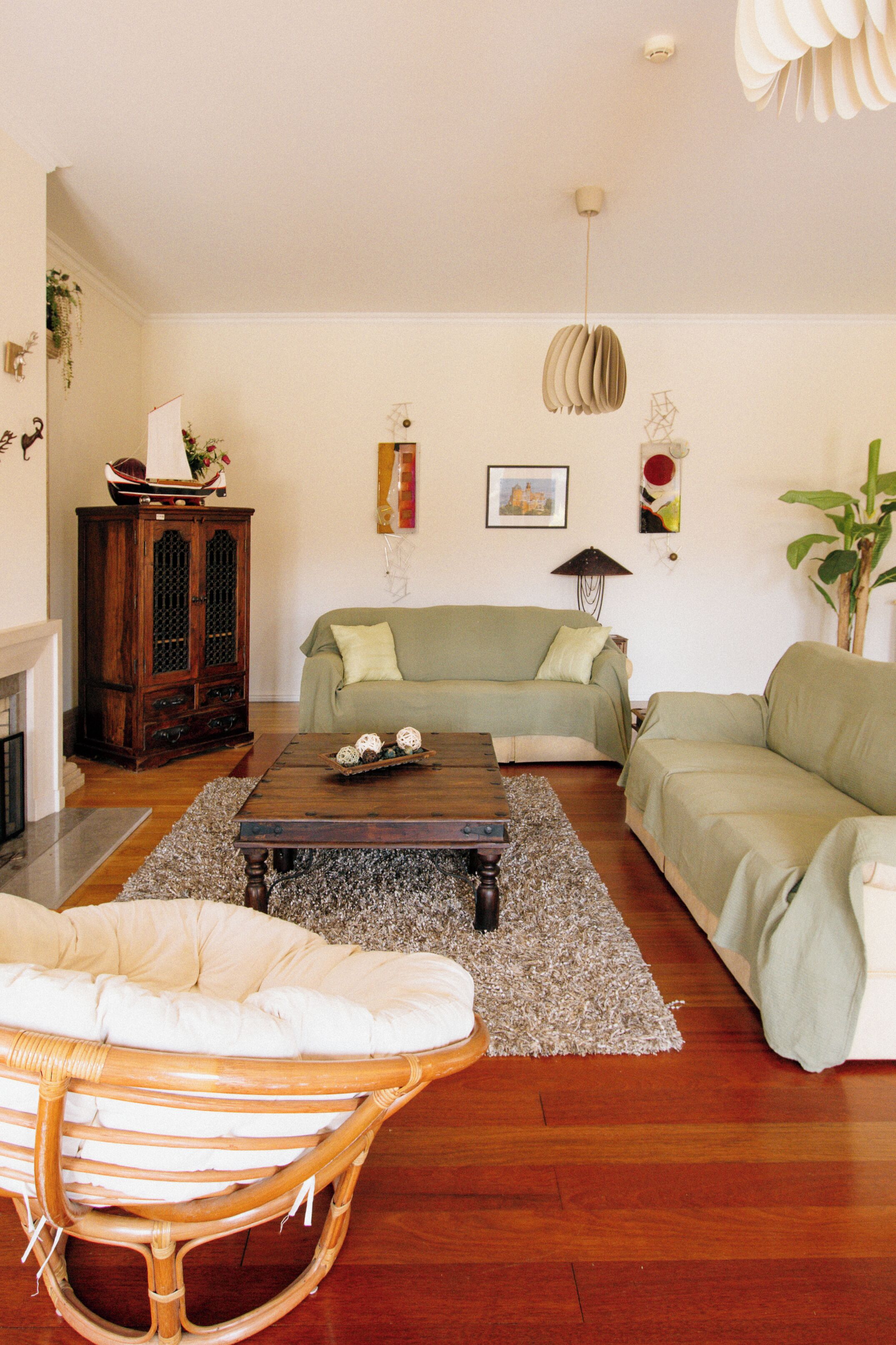 A living room with a wooden coffee table, two green sofas, a wicker chair, and a cabinet.