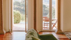 Une pièce avec un canapé vert, donnant sur un patio avec une table et des chaises, et une grande fenêtre offrant une vue sur la verdure.