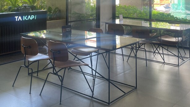 A modern conference room with glass tables and chairs, large windows with a view of greenery and a parking area, and a reception desk labeled "TA KAPI". - Modern Studio | Fast WiFi, Netflix | Short walk to IT Park (Cebu City)