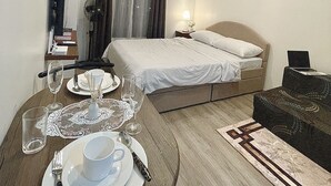 A hotel room with a bed, bedside table with a lamp, a small table with a cup and saucer, and a chair. - Modern Studio | Fast WiFi, Netflix | Short walk to IT Park (Cebu City)