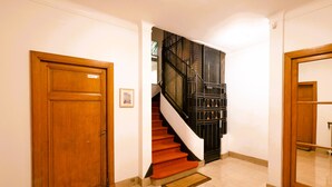 A hallway with a wooden door, a staircase with red carpet, and a black metal railing.