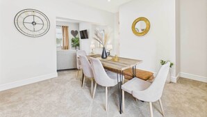 Un coin repas comprenant une table en bois, quatre chaises rembourrées, une horloge murale, un téléviseur et un miroir.