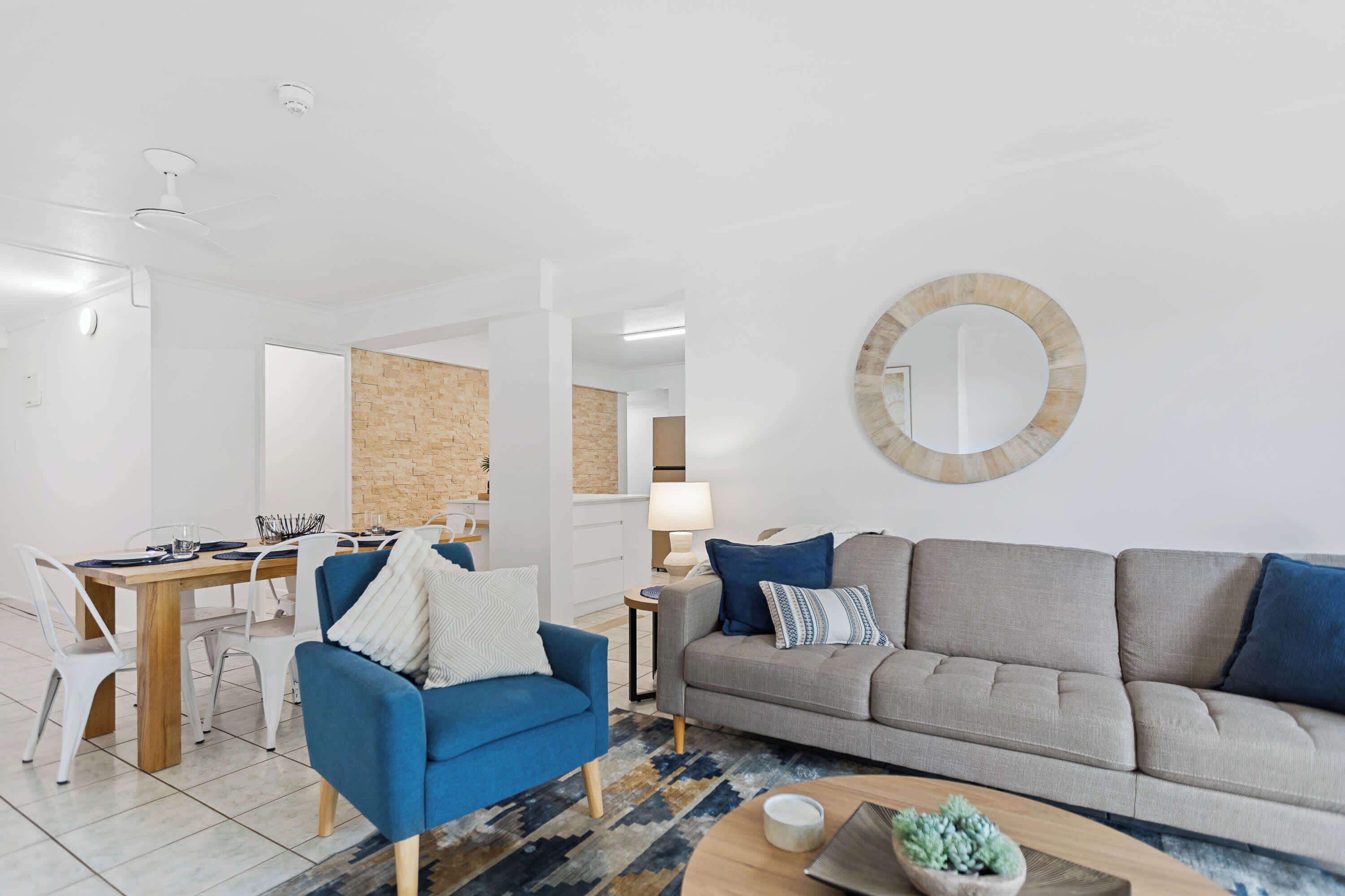 Un salon moderne avec un fauteuil bleu, un canapé gris et un miroir rond accroché au mur.