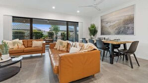 Una sala de estar moderna con un sofá de cuero marrón, una mesa de comedor con sillas y un amplio ventanal con vistas a un jardín.