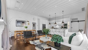 Un salon spacieux doté d’un parquet, d’une table basse ronde, d’un canapé blanc et d’un coin repas avec une table en bois et des chaises noires.