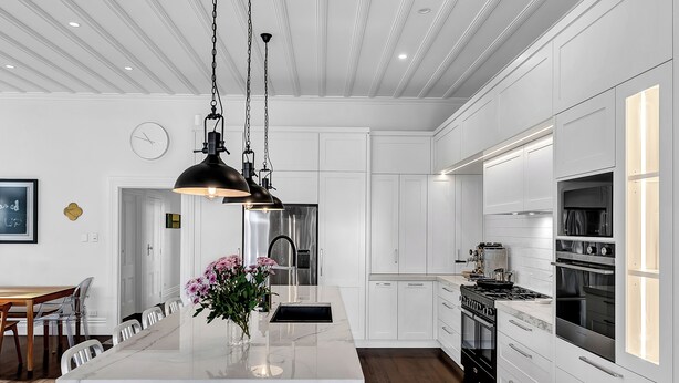 Une cuisine moderne avec des meubles blancs, un îlot en marbre, des appareils en acier inoxydable et des luminaires suspendus.