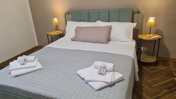 A neatly made bed with white linens, two bedside lamps, and towels on the bed. - Verdi HOUSE - Relaxation and Flavors (Savigliano)