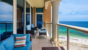 A balcony with a view of the ocean, furnished with a sofa, chairs, and a table.
