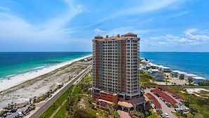 A high-rise hotel with a beach view, featuring multiple balconies and a parking area.