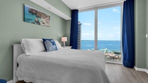 Un dormitorio con una cama grande, vista al mar y un paisaje urbano de fondo.