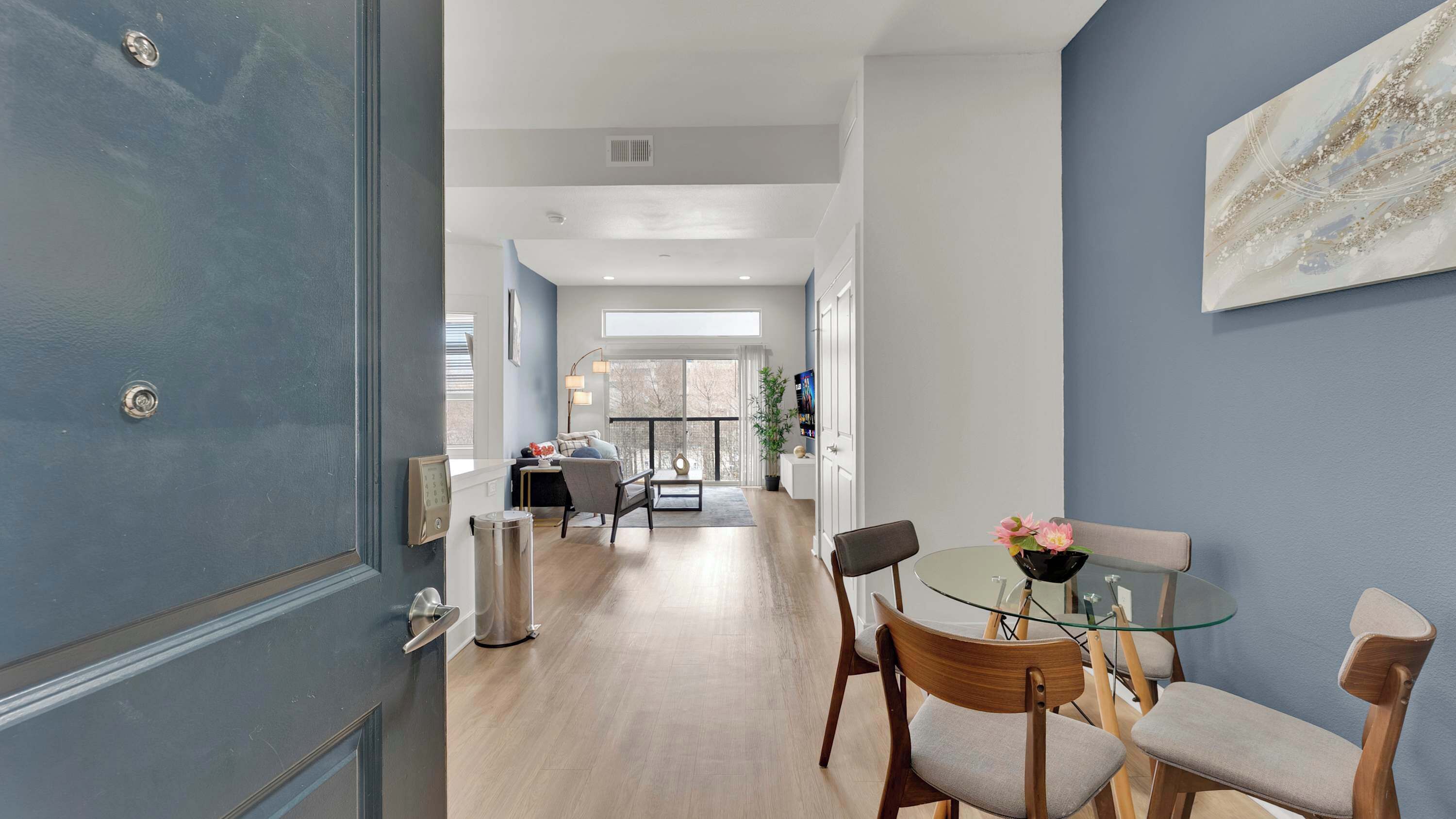 A modern interior with a dining area, a living room, and a hallway leading to a balcony.