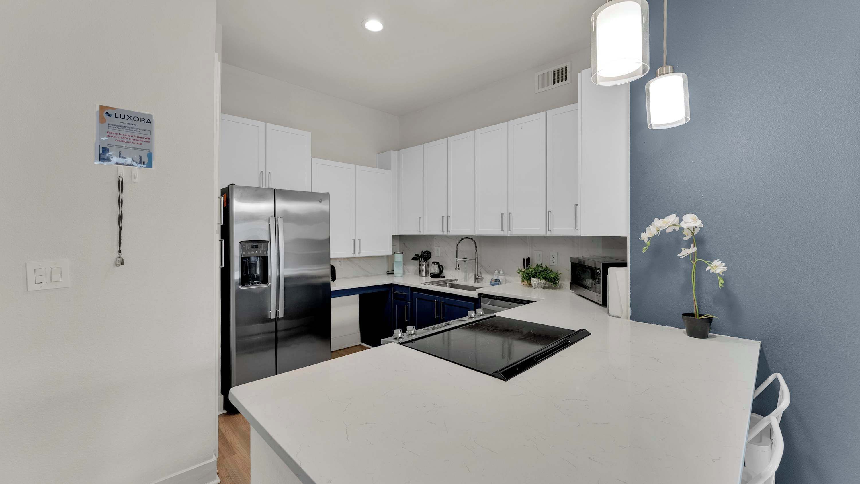 A modern kitchen with white cabinets, a stainless steel refrigerator, a built-in oven, and a central island with a sink.