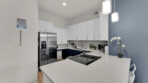 A modern kitchen with white cabinets, a stainless steel refrigerator, a built-in oven, and a central island with a sink. - Plush 2BR Dallas Flat | Pool Gym Parking (Dallas)