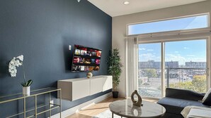 Un salon moderne doté d’un grand téléviseur fixé au mur, d’un canapé, d’une table basse et offrant une vue sur la ville grâce à de grandes fenêtres.