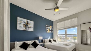 Une chambre d’hôtel avec deux lits, un ventilateur de plafond, une fenêtre avec des stores et des œuvres d’art accrochées aux murs.