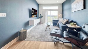 Een moderne woonkamer met een blauwe accentmuur, een flatscreen televisie, een bank, een salontafel en uitzicht op het groen.