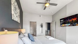 Een moderne hotelkamer met een groot bed, een plafondventilator, een aan de muur bevestigde televisie en een deur naar een eetgedeelte.