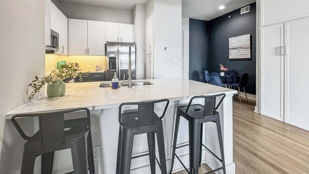 Een moderne keuken met witte kasten, een roestvrijstalen koelkast en een marmeren kookeiland met barstoelen.