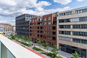 A modern multi-story building with a mix of brick and glass facades, surrounded by a landscaped area with trees and a red pathway.