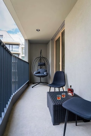 A balcony with a hanging chair, a table with two glasses, and a bottle of liquor.