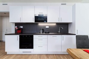 Uma cozinha moderna com armários brancos, forno embutido, máquina de café e pia.