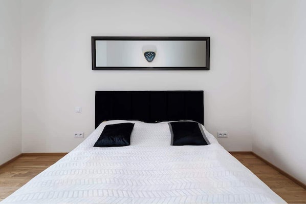 A neatly made bed with a white quilt and two black pillows, a black headboard, and a framed emblem on the wall above.