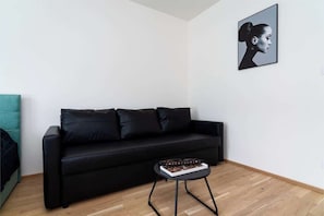 A modern living room with a black sofa, a small round table with a tray of chocolates, and a framed portrait on the wall.